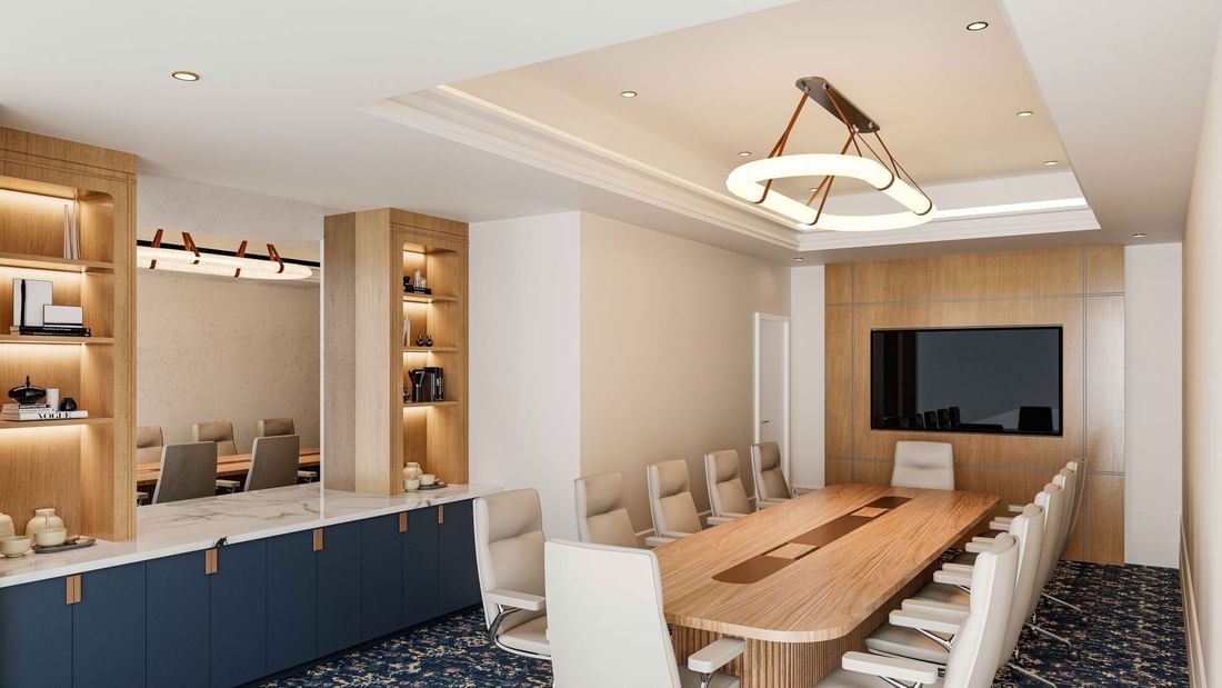 Modern boardroom at El Prado Hotel, with a long wooden table, comfortable chairs, and a large screen