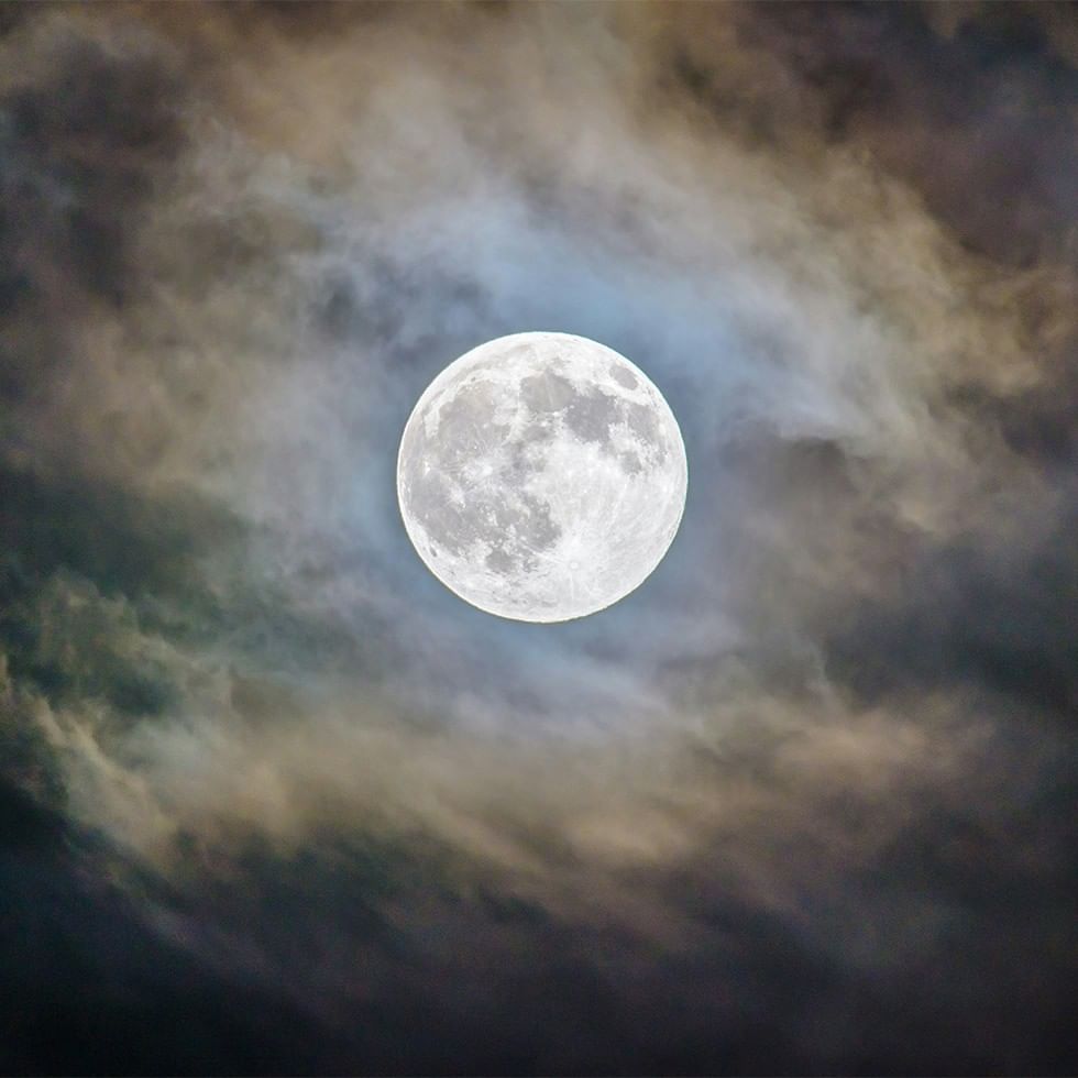 Luna piena illuminata tra nuvole scure in una notte tempestosa.