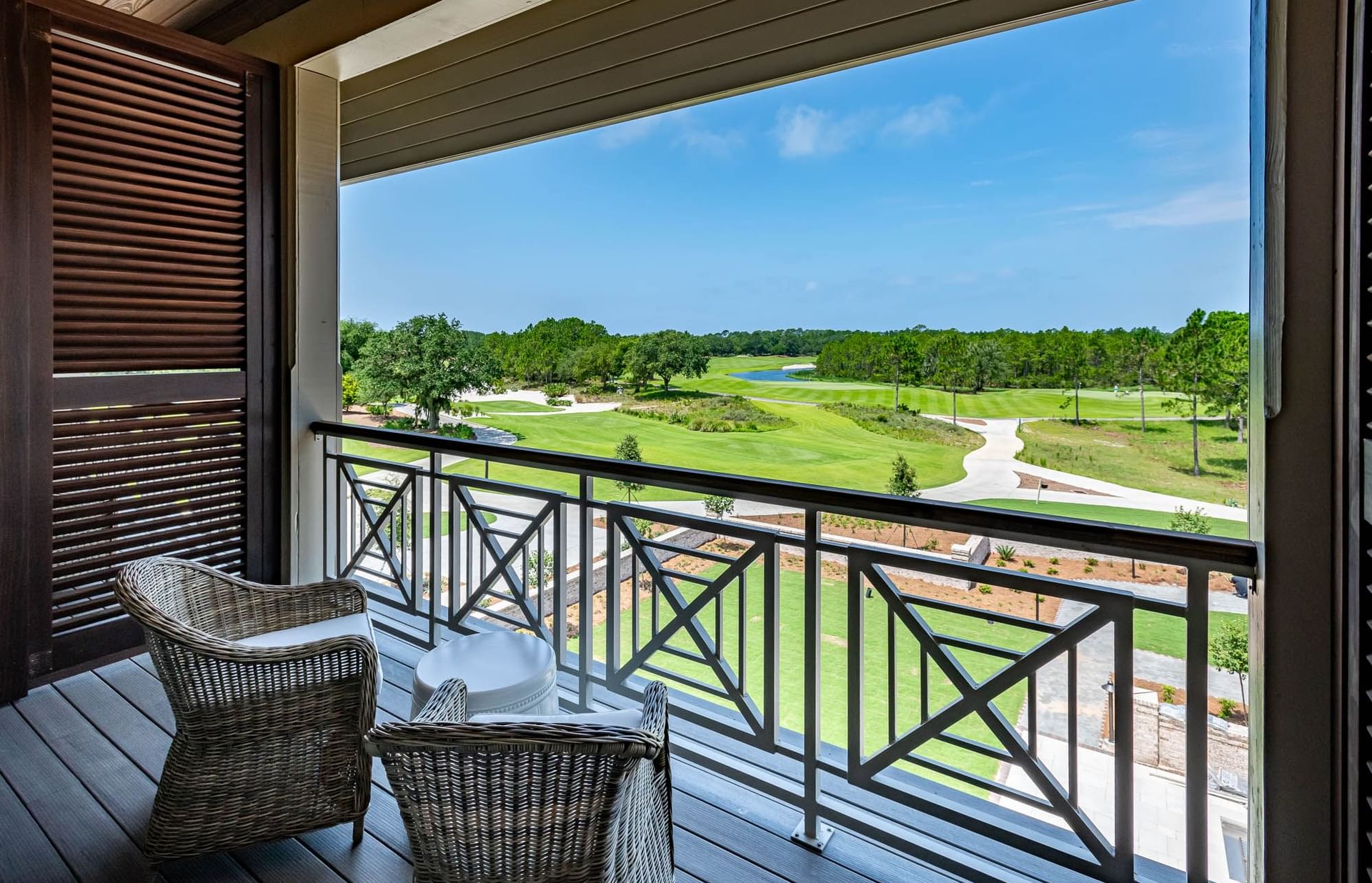 Balcony with two wicker chairs and a view of a golf course and trees.
