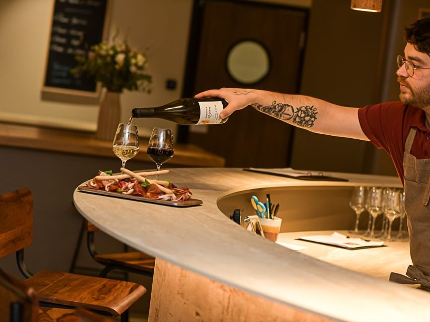 Serveur versant du vin au comptoir avec des plats de charcuterie à l'Hôtel Rivella.