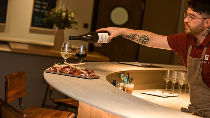 Serveur versant du vin au comptoir avec des plats de charcuterie à l'Hôtel Rivella.