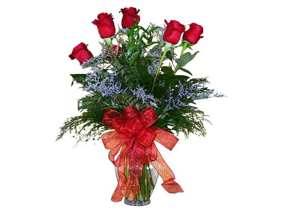 A half dozen roses arranged in a vase with a red bow