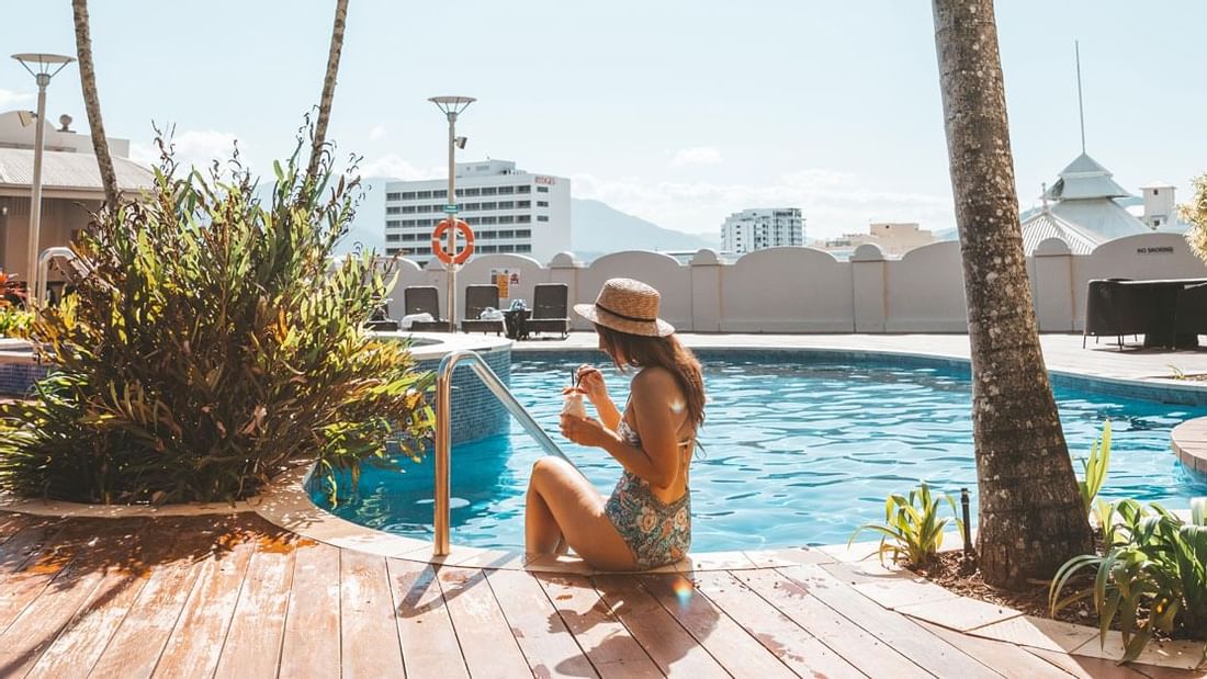 A lady sitting by a pool & having a drink at Pullman Cairns