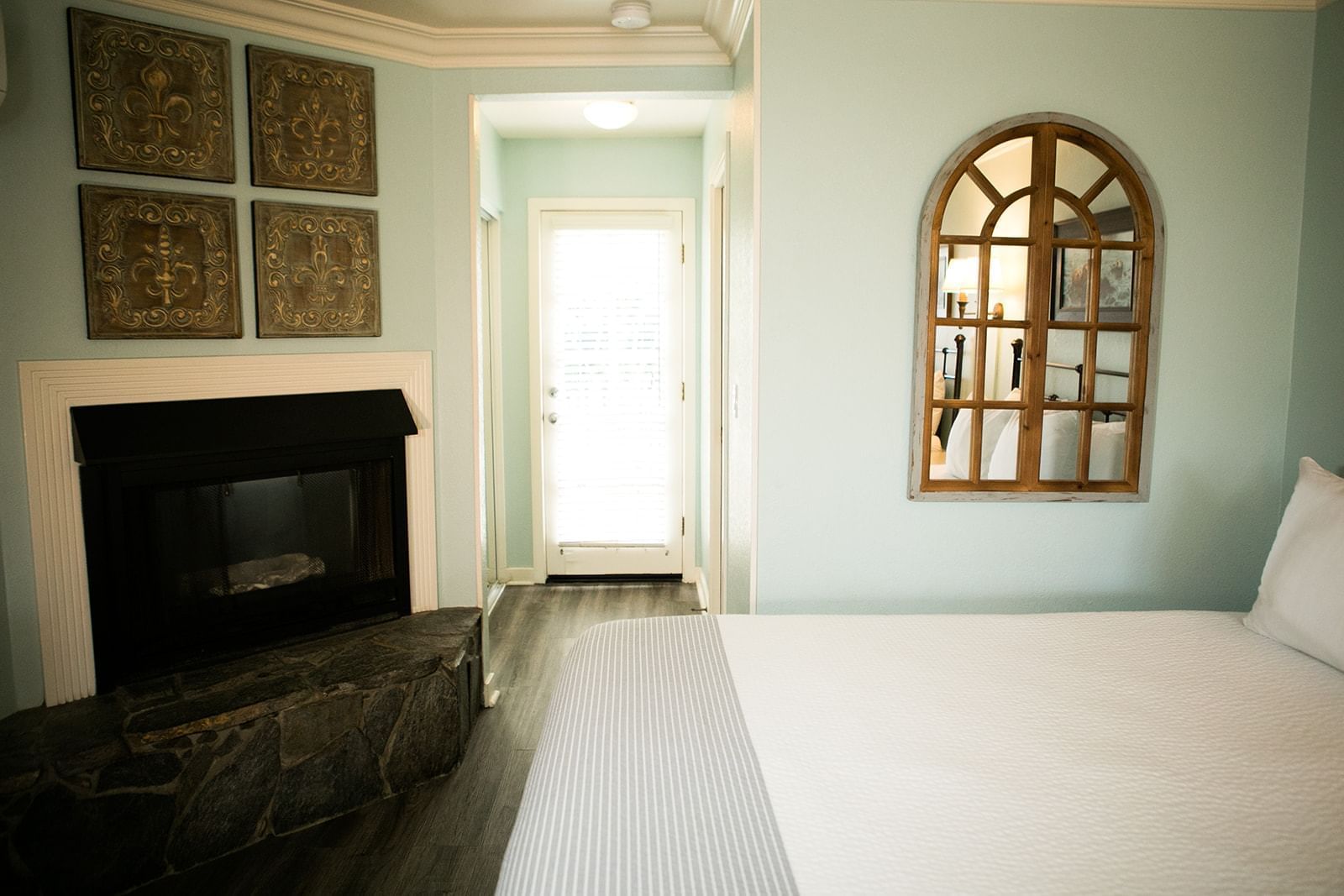 A hotel room with a queen bed, fireplace, and window mirror