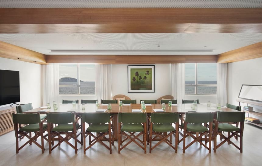 Área de eventos com restaurante à beira-mar do Janeiro Hotel, com mesa para reunião e TV