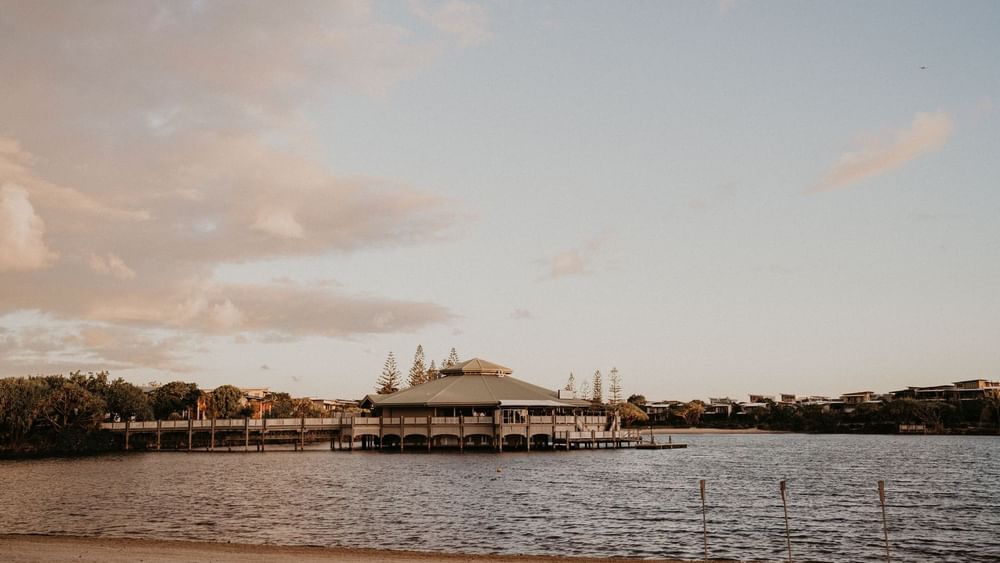 Exterior view of Lily’s on the Lagoon surrounded by trees and calm water at Novotel Sunshine Coast Resort