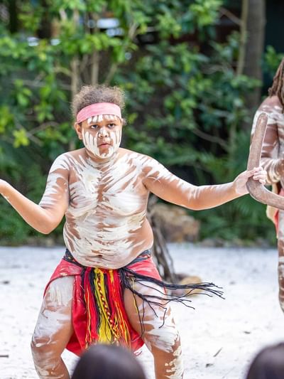 First Nations people in traditional dress and body paints performing on a beach near Sofitel Brisbane Central