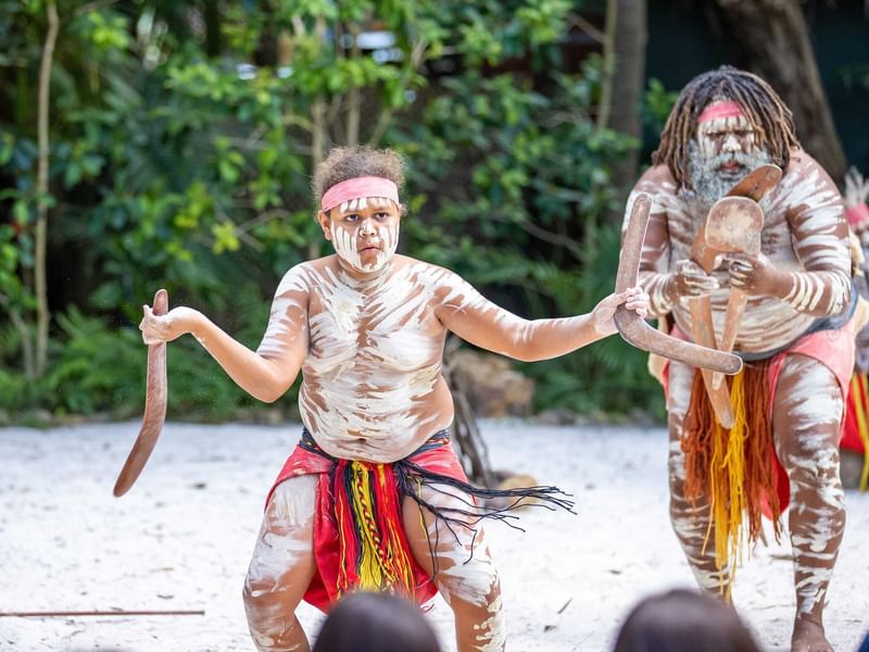 First Nations people in traditional dress and body paints performing on a beach near Sofitel Brisbane Central