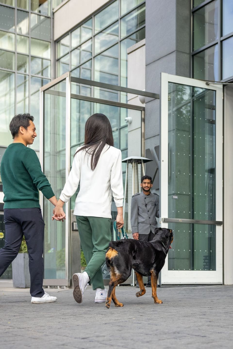 Couple walking Rottweiler toward entrance door beside staff member greeting guests outside at Hotel X Toronto
