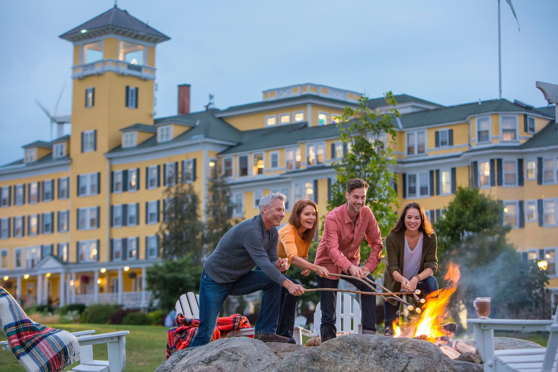 Family toasting wine glasses by a fire pit on boulders, near Adirondack chairs, at Mountain View Grand Resort & Spa