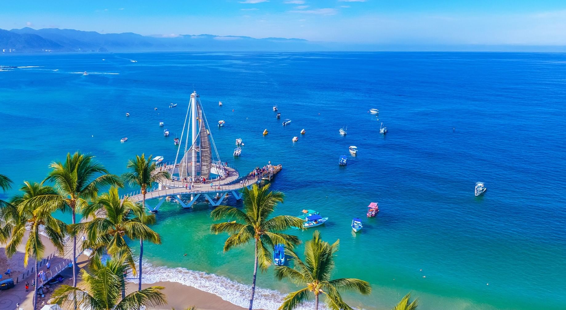 Aerial view of the sail-shaped pier, surrounded by blue ocean water and boats near Playa Los Arcos Beach Resort & Spa