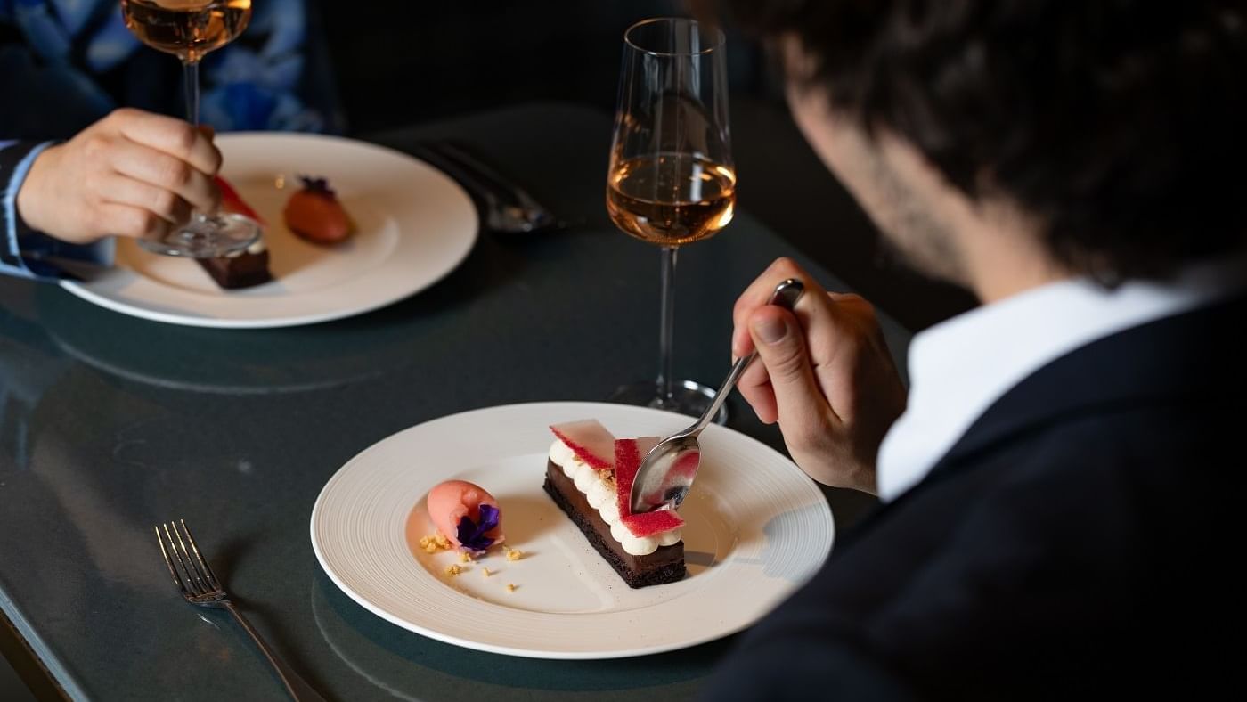 Two people enjoying dessert on a plate served with a glass of wine at The Londoner Hotel