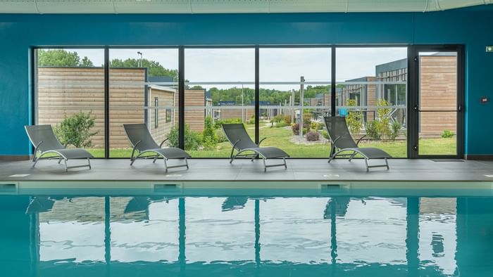 Indoor pool with sun loungers at The Originals Hotels