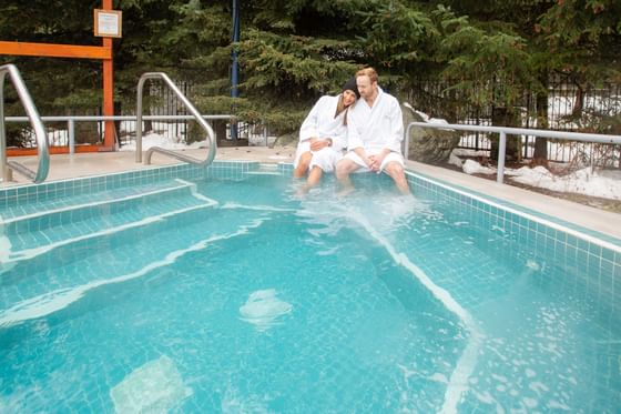 Couple lounging on the outdoor jacuzzi edge at Blackcomb Springs Suites