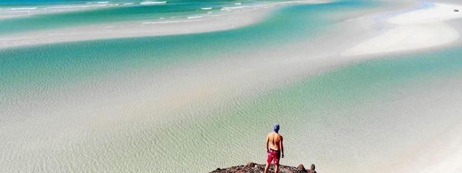 Man standing on a rocky outcrop overlooking a stunning white sand beach at Marquis Los Cabos Resort
