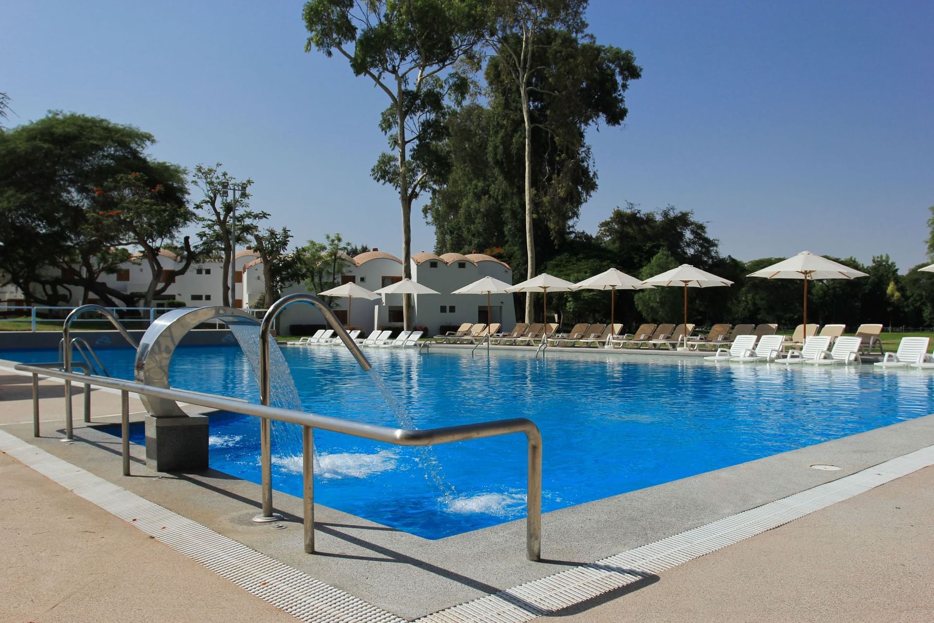 A sunny pool featuring blue water, lounge chairs and umbrellas at Las Dunas Resort Ica