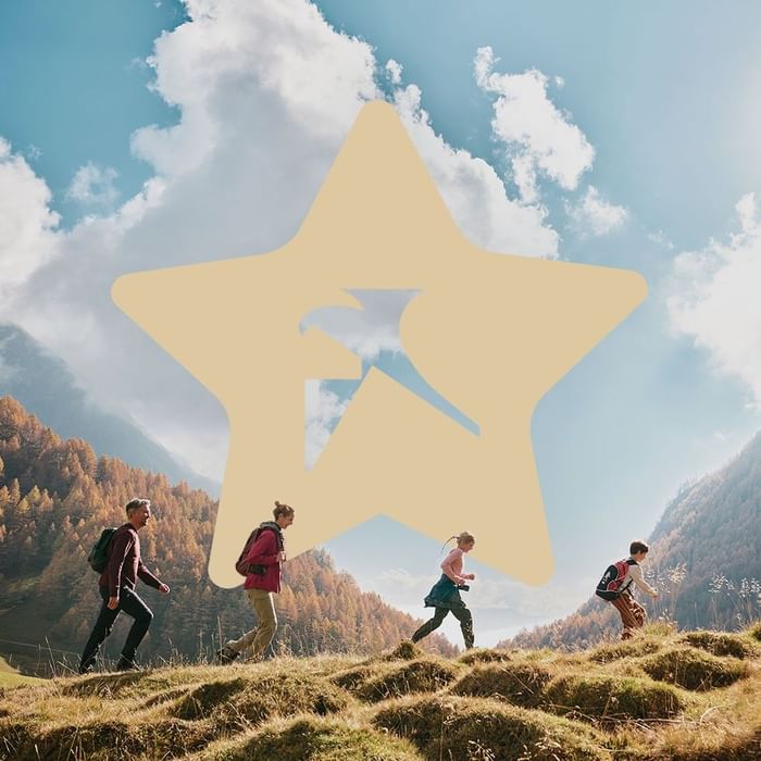 Četiri osobe s ruksacima idu prema planini, prekriveno oblacima s velikom zvijezdom u sredini.