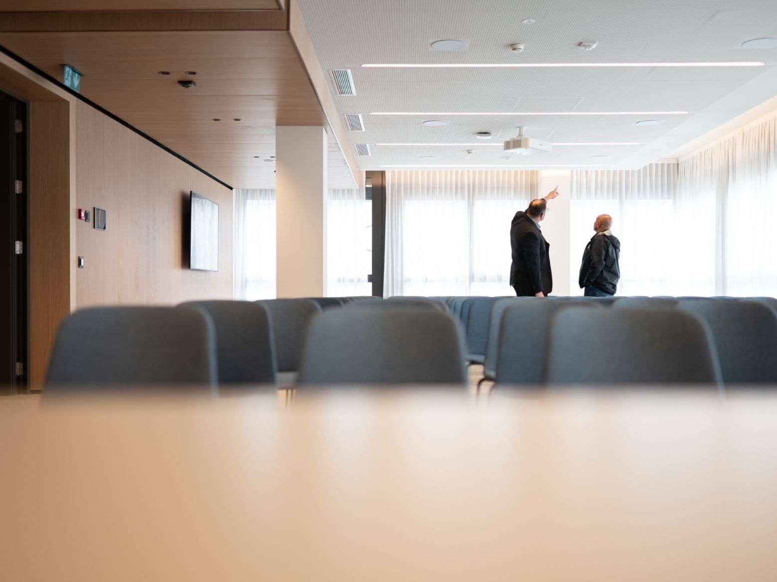 Two individuals view a bright presentation space at Hotel des Innovations with tiered seating and sheer curtains
