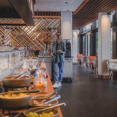 Frau wählt Gerichte an einem Buffet in einem hellen, modernen Restaurant mit vielen Sitzplätzen.