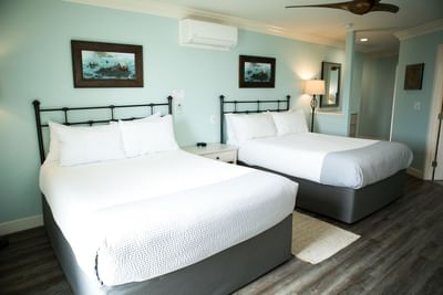 Two beds with white bedding, wooden frames, and framed artwork above, in a room with blue walls and wooden floors.