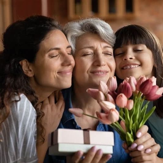 Family picture of a grandma, mum and daughter smelling some flowers