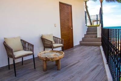 Outdoor terrace with wicker chairs, wooden table, and ocean view staircase at Playa Los Arcos Puerto Vallarta