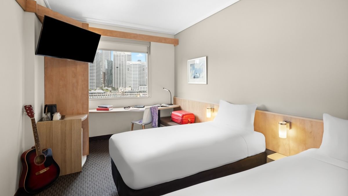 Superior room with two single beds, work desk, wall-mounted TV, and city skyline view at Ibis Sydney Darling Harbour