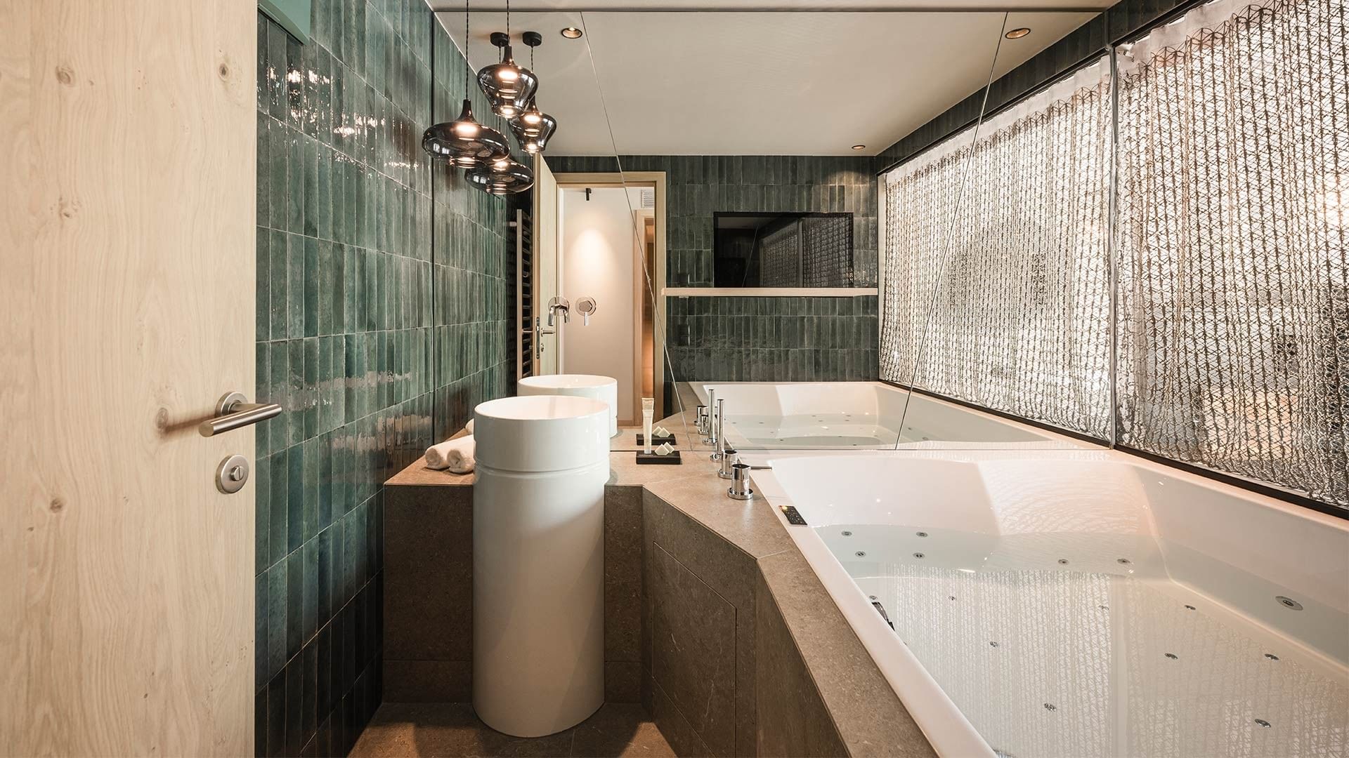 Modernes Badezimmer mit freistehender Badewanne, zwei Waschbecken und grünen Fliesen.
