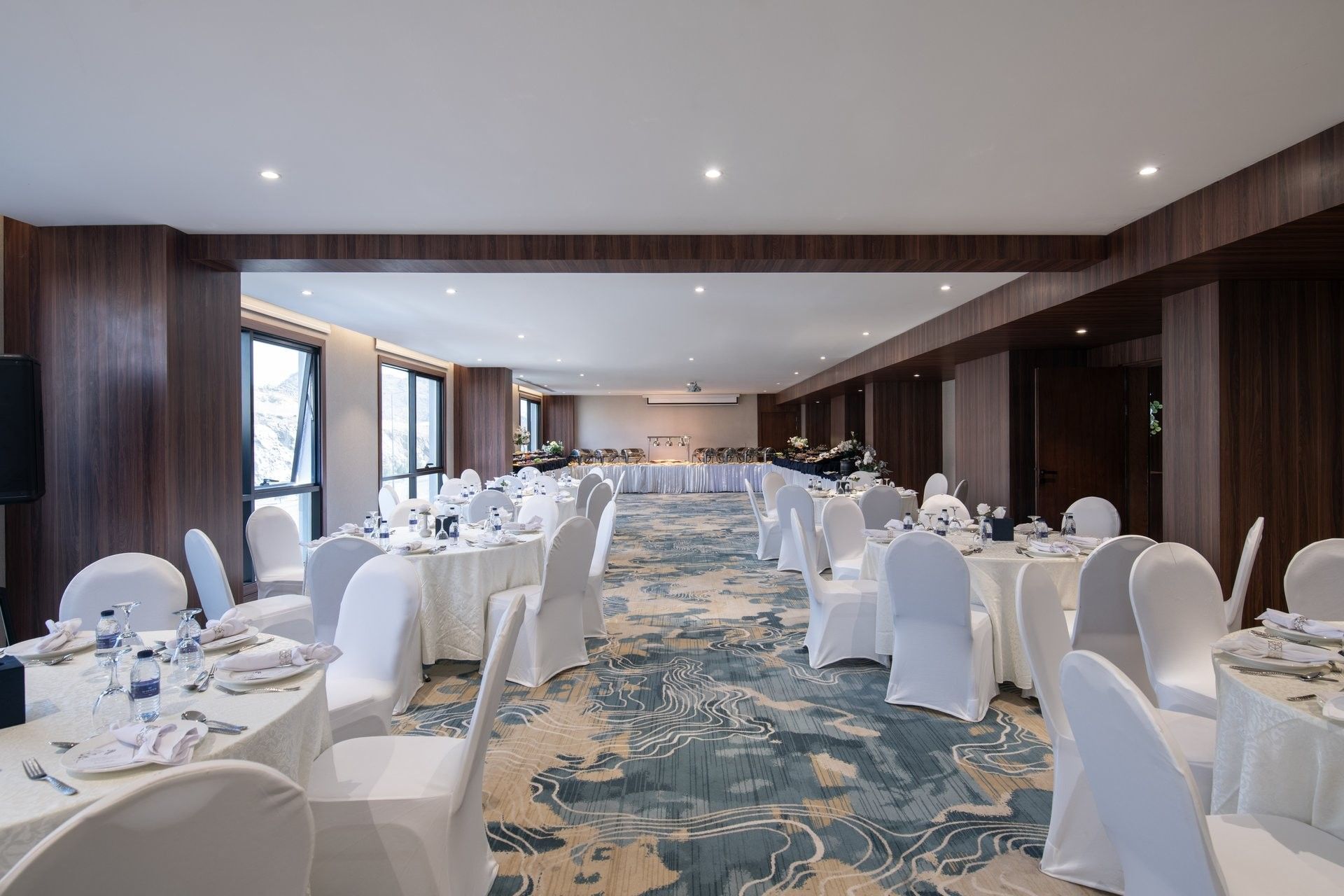 Banquet tables surrounded by white-clothed chairs under recessed lights in Amarige hall at Warwick Al Taif Hotel