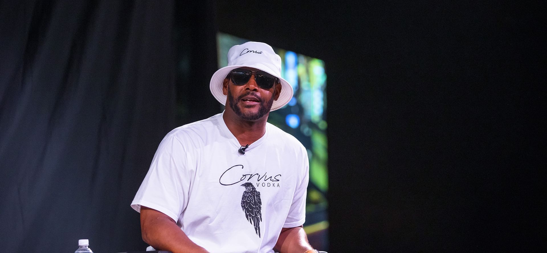 Former NFL player Kam Chancellor wearing white bucket hat and sunglasses at event on stage venue at The Brook