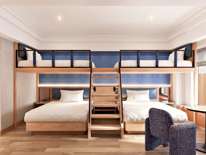 Two loft beds above twin beds with a wooden ladder and an armchair in the Mountain View Family Loft Room at Grand Park Otaru