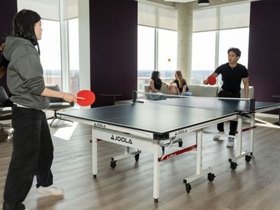 Students having fun playing ping pong in a bright games room with floor to ceiling windows.