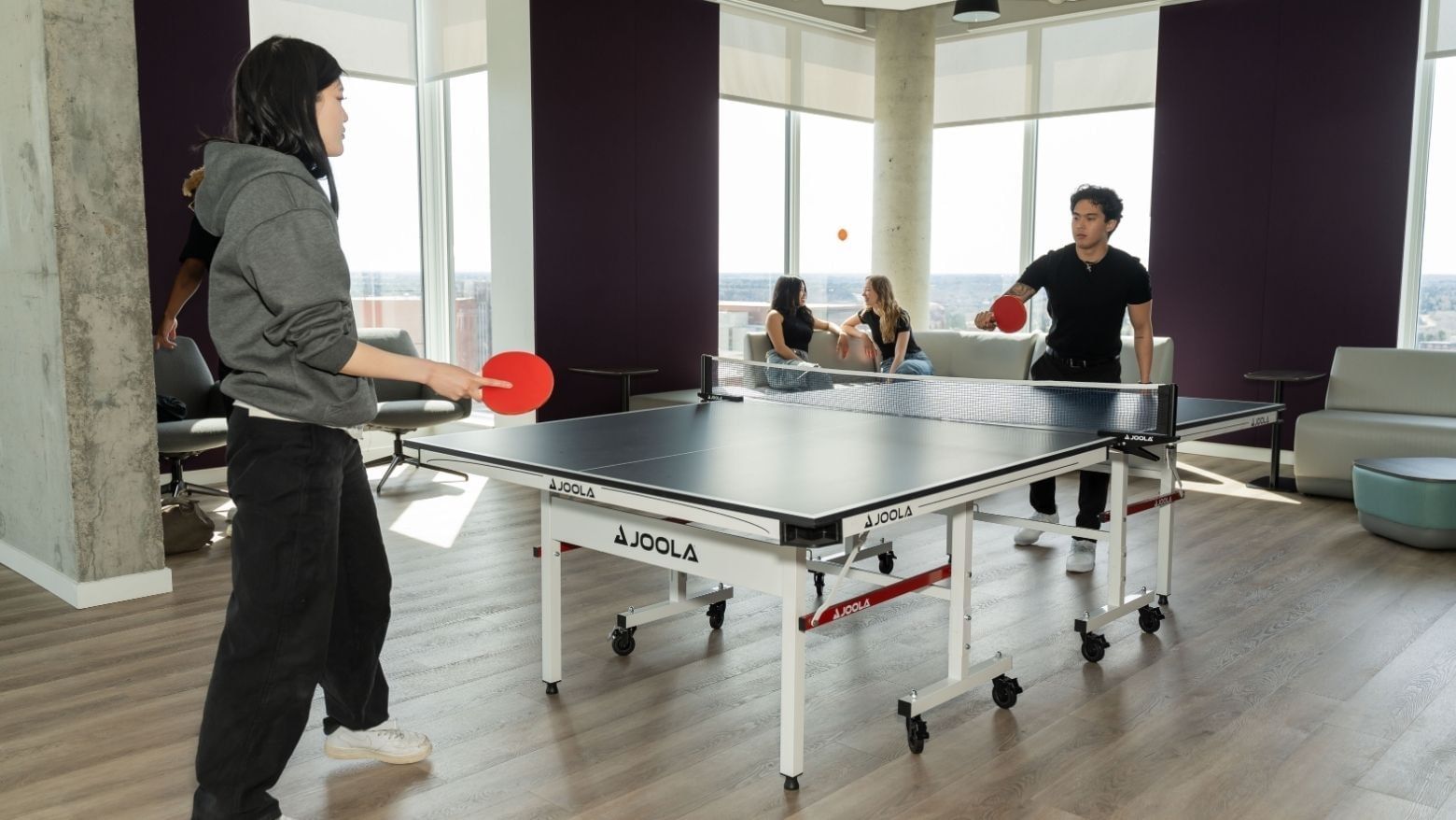 Students having fun playing ping pong in a bright games room with floor to ceiling windows.