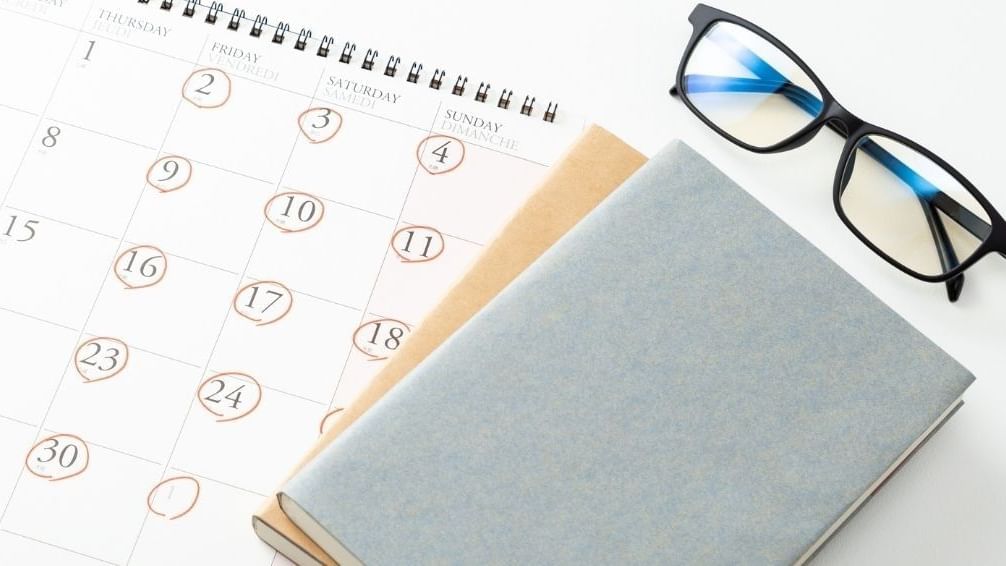 A calendar, glasses, and a book on a desk for planning an adventure-fuelled weekend.