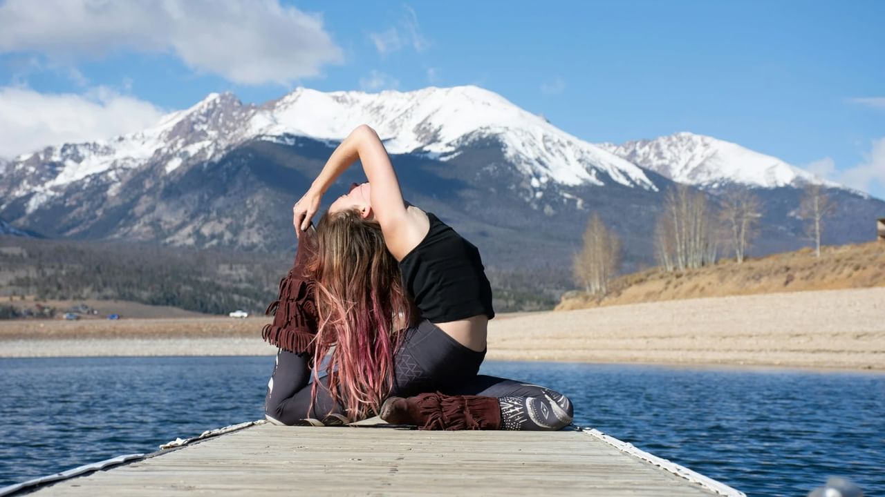 A person practices a yoga pose on a dock in front of the mountains in Canmore.