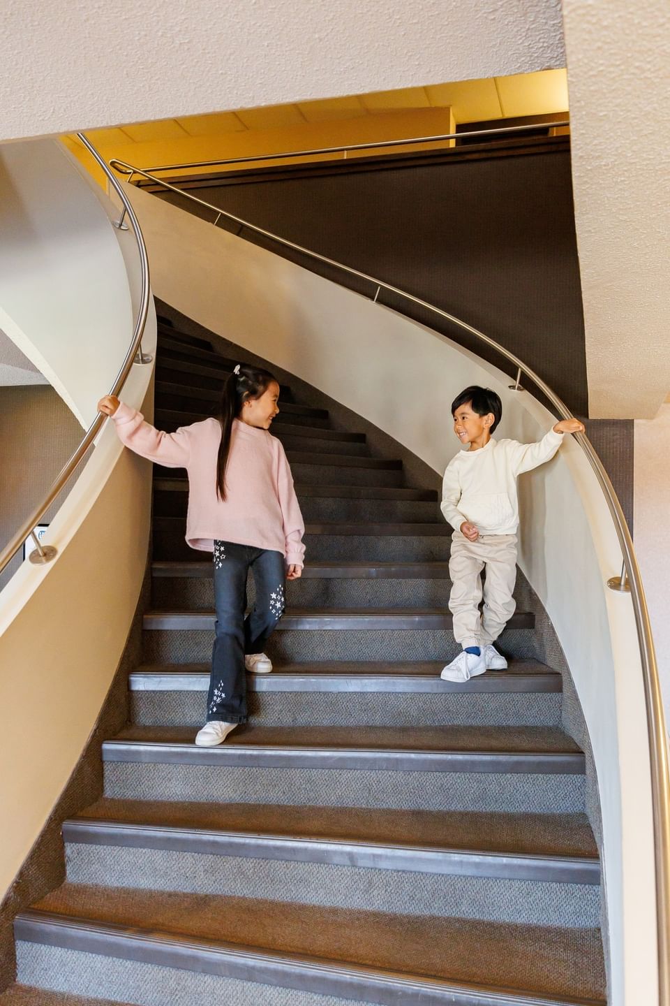Two happy young children walking down a grand winding spiral staircase with steel handrails at Rodd Royalty