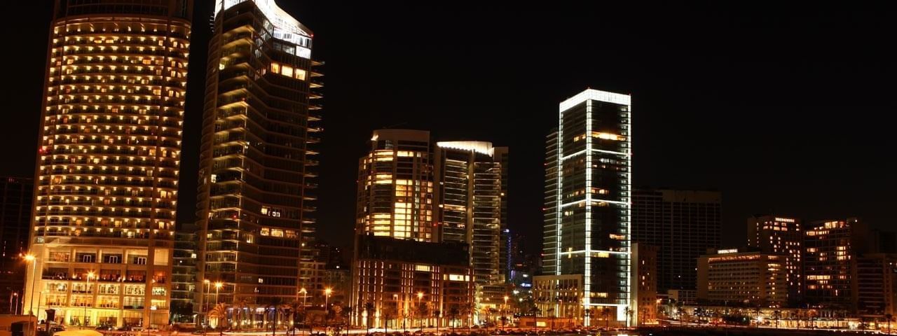 City skyline at night with glowing lights in tall buildings under a dark sky near Warwick Palm Beach Hotel
