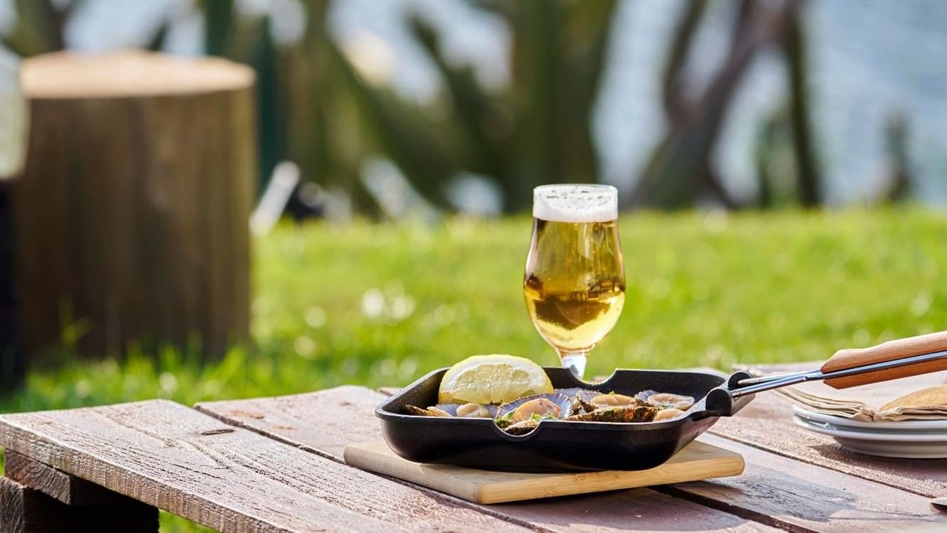 Pan of fresh mussels with a lemon wedge & a glass of beer, served on a wooden table in Caloura Terrace Bar at Bensaude Hotels