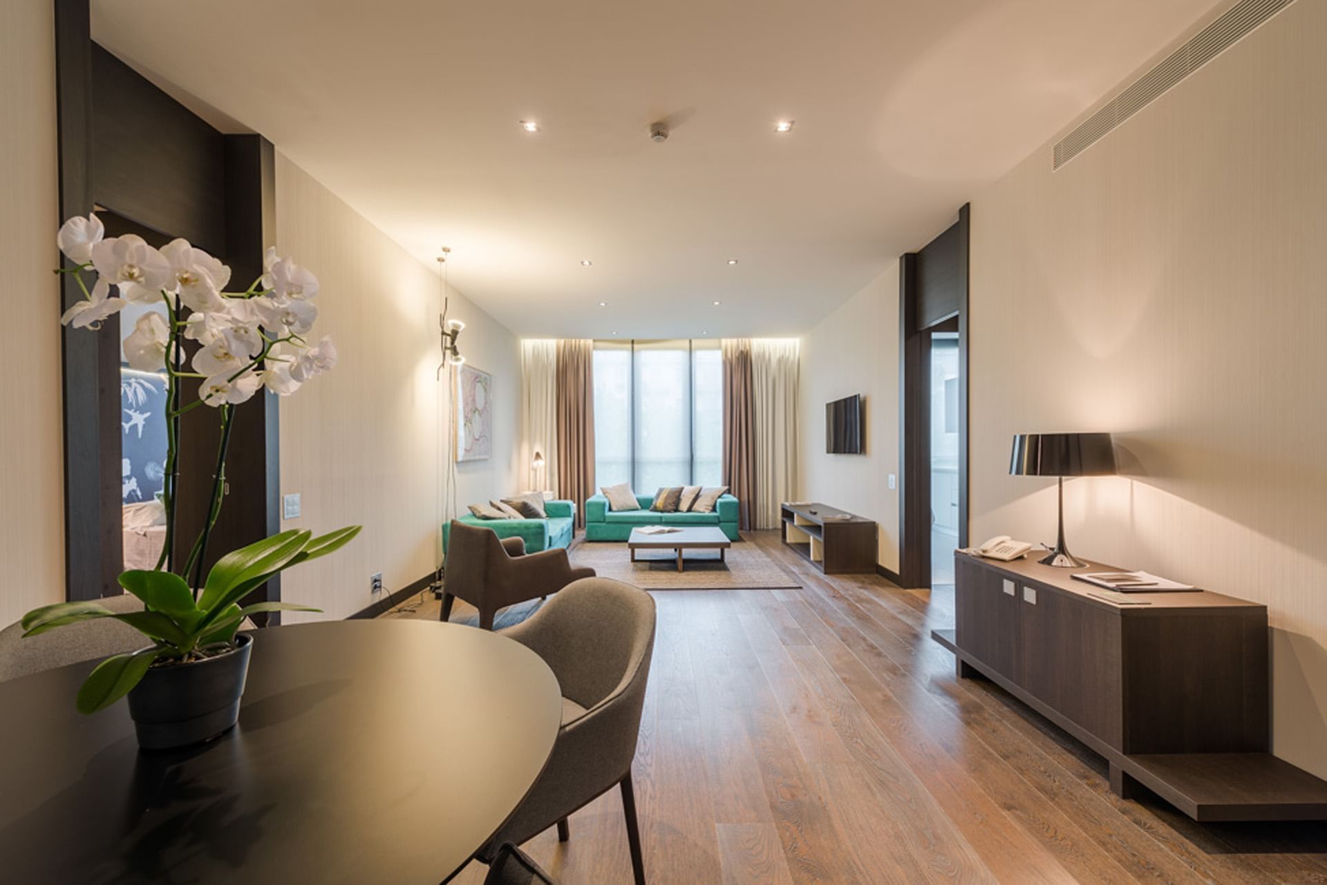 Elegante suite con tavolo, divano verde, libreria, lampada, pavimenti in legno e fiori di orchidea a DUPARC