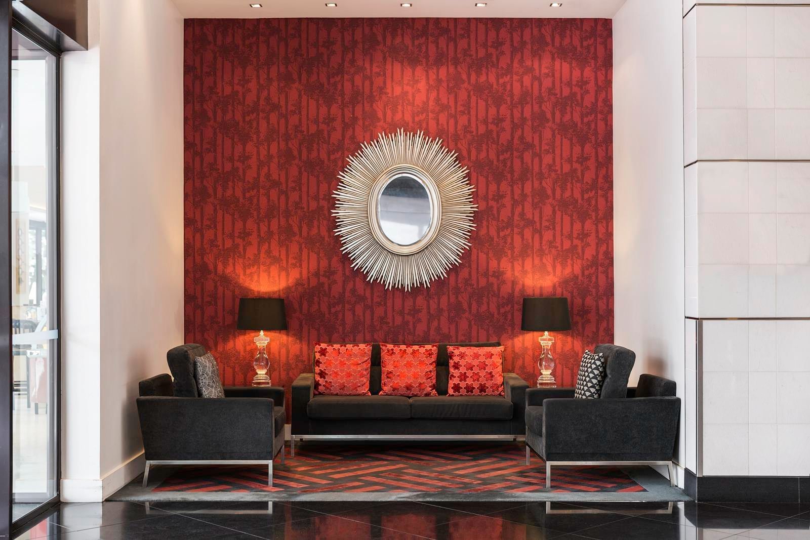 Sofa with three red cushions, flanked by two armchairs and two lamps, at The Sebel Auckland Viaduct Harbour