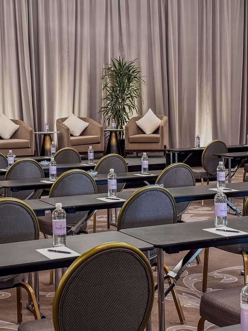 Rows of desks by round-back chairs under a curtained stage in Turtle Creek Ballroom B at Warwick Melrose Dallas