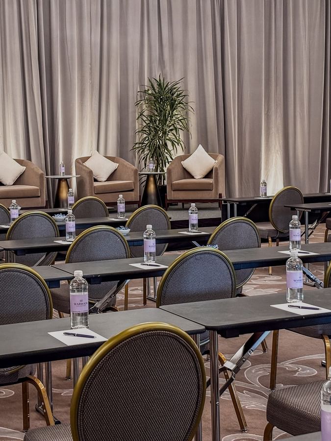 Rows of desks by round-back chairs under a curtained stage in Turtle Creek Ballroom B at Warwick Melrose Dallas