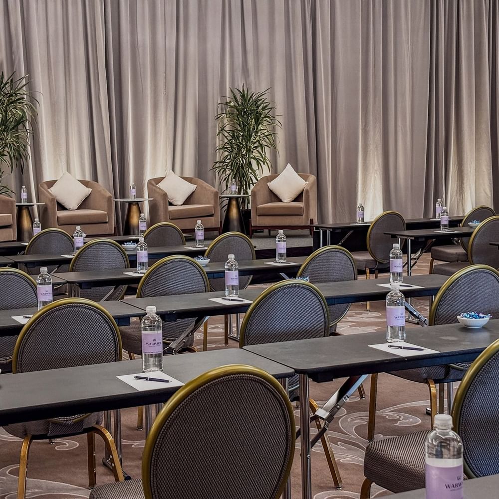 Rows of desks by round-back chairs under a curtained stage in Turtle Creek Ballroom B at Warwick Melrose Dallas