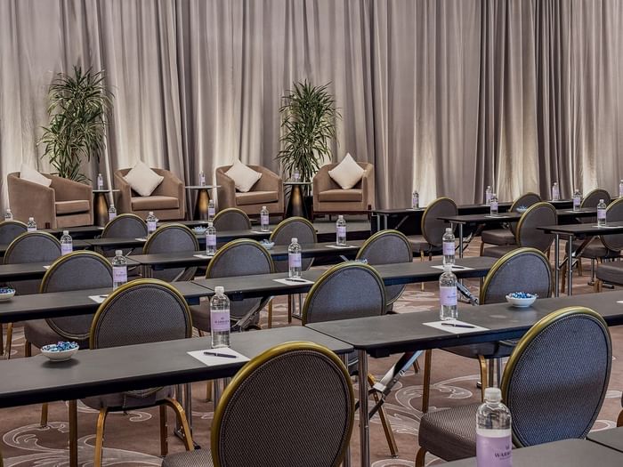 Rows of desks by round-back chairs under a curtained stage in Turtle Creek Ballroom B at Warwick Melrose Dallas