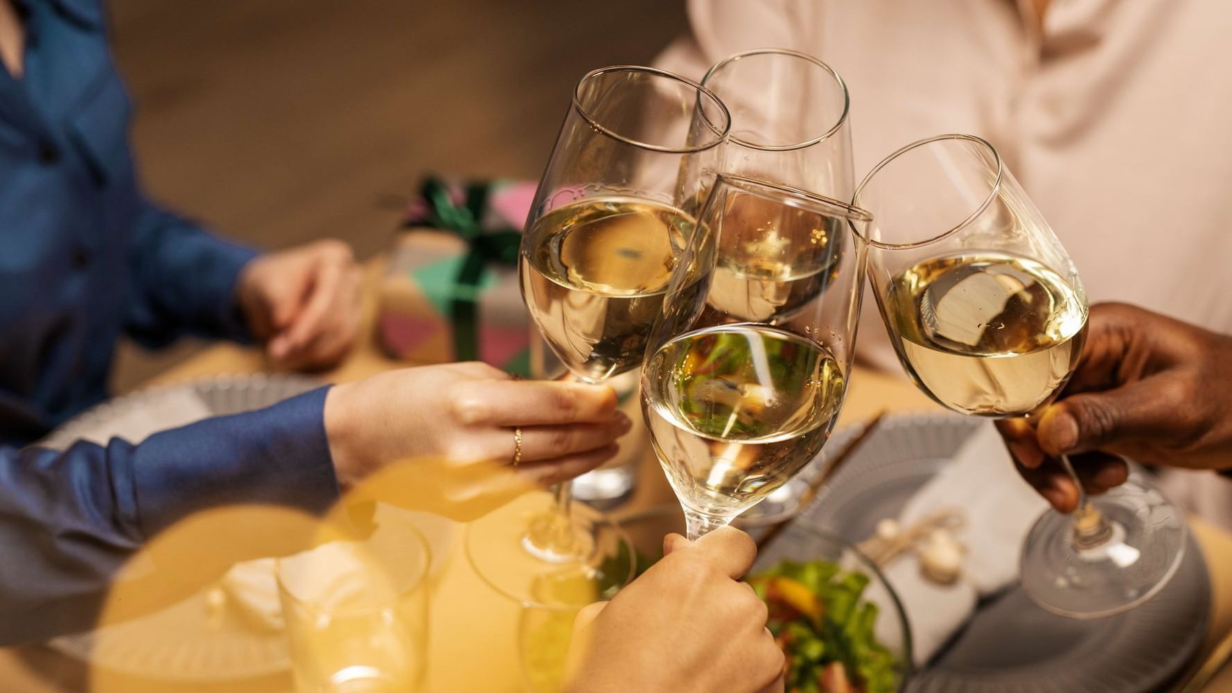 Close-up of hands toasting with glasses of white wine, surrounded by a festive table setting at Paramount Hotels