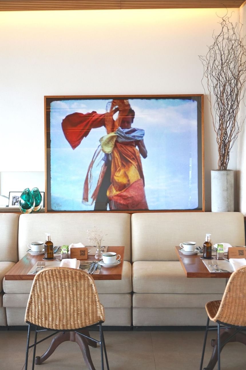Um dos espaços do Janeiro Hotel onde o serviço de café da manhã é servido aos hóspedes, decorado com poltronas, mesas e um lindo quadro na parede ao lado de um vaso decorativo