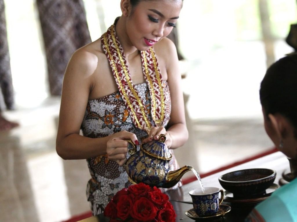 A lady dressed in traditional clothes pouring tea for a guest at Patehan Royal High Tea in Royal Ambarrukmo Yogyyakarta
