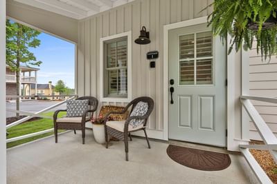 Stylish porch with wicker chairs and a Cottage 1 entrance door in a calm garden setting by Cottages at Laurel Brooke