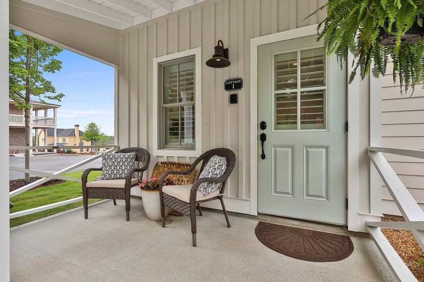 Stylish porch with wicker chairs and a Cottage 1 entrance door in a calm garden setting by Cottages at Laurel Brooke