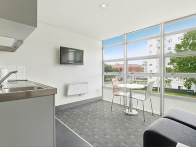 Modern room with kitchen sink, TV, and dining table with city view at Student Living Auckland - Beach.
